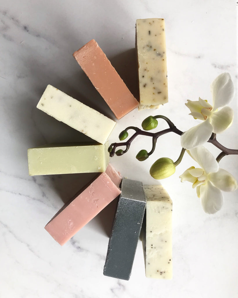 A half circle of soaps in shades of pink, gray and speckled beige on a marble background. 